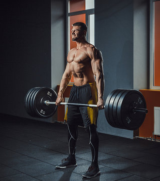 european caucasian athletic man doing deadlift with heavy barbell. man lifting barbell opposite window. emotional moment of lifting weight. affective lifting in gym. posing in gym
