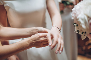 bridesmaids dressing bride in the morning in hotel  room. girls helping bride put on stylish silver bracelet. view at hands