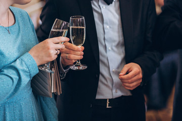 group of elegant people holding glasses of champagne at luxury wedding reception. people hands toasting and cheering with drinks at social events.  christmas celebration