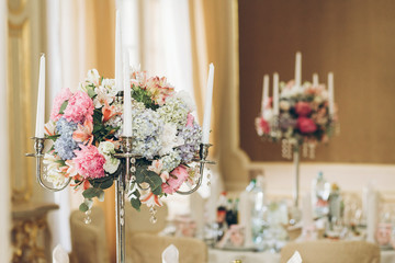 beautiful hydrangea bouquets in vases and shiny silver candelabras with candles on tables at luxury wedding reception in restaurant. stylish decor and adorning