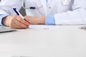 Female doctor filling up prescription form while sitting at the desk in hospital closeup.  Physician finishing up examining his patient in hospital and ready to give an advice to help. Healthcar