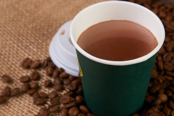 Green Take away coffee cup with roasted coffee beans on wooden background, close-up