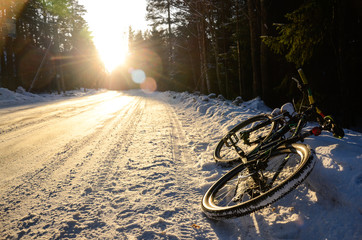 Mountain bicycle on the snowy road in winter forest at sunset