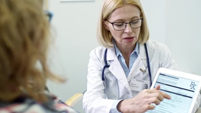 Tilt up of mature physician showing test results on tablet to unrecognizable patient and explaining diagnosis; name Helen Brown in used in fictitious manner