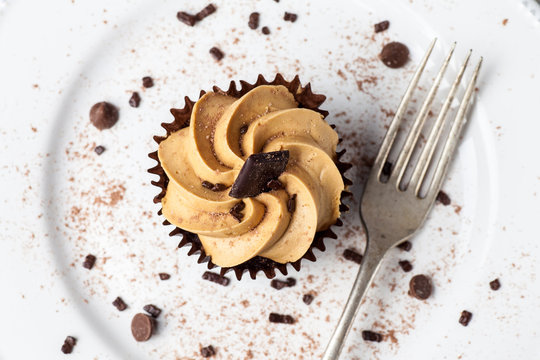 Salted Caramel cupcake on white plate with fork, dusted with cocoa powder and chocolate sprinkles, Overhead View