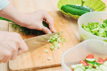 Close-up of gentle female hands slice on the wooden board the stalks of green onions making salad. The concept of a vegetarian healthy food and lifestyle. Making healthy food at home