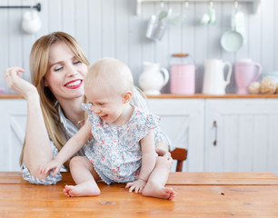 Young mother playing with her baby daughter in a modern kitchen setting. so cute family. Funny girl with mom on kitchen.