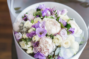 Flower in transparent plastic box. Brides wedding bouquet with peonies, freesia and other flowers on black arm chair. Light and lilac spring color. Morning in room