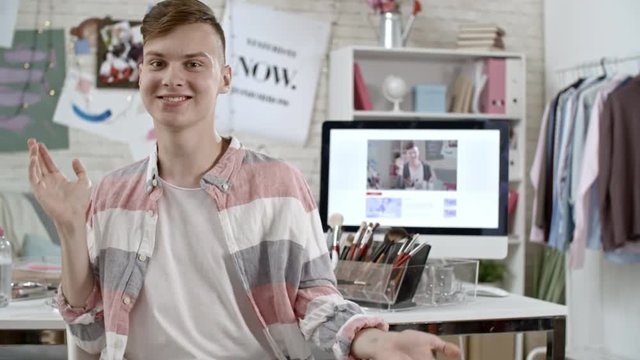 Medium shot of cheerful male teenage fashion blogger looking at camera and gesturing while talking to his viewers