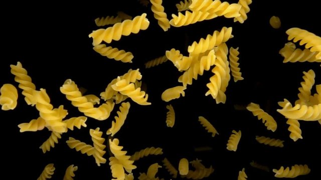 Pasta fusilli bouncing against to the camera on a black background in slow motion