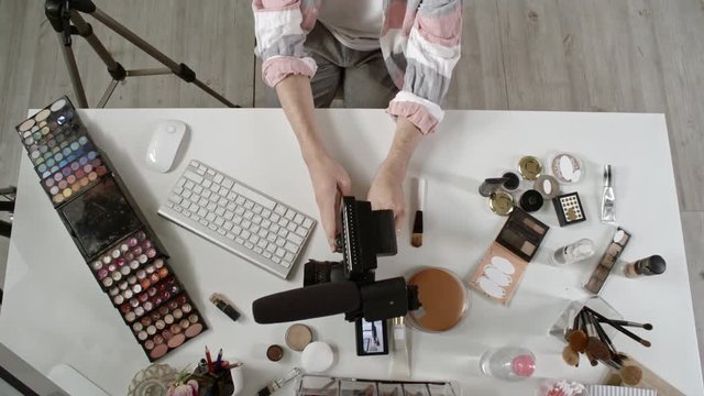 Crane shot with top view of male teenage beauty blogger sitting at his desk and taking SD card out of video camera with microphone, then inserting it into computer and working