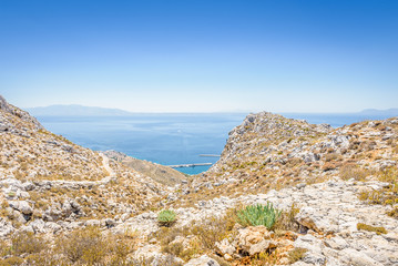 Fototapeta na wymiar Beautiful sunny holiday view to the greek beach blue sea with crystal clear water beach with some boats fishing cruising surrounded by hills mountains, Kalymnos Island, Kos, Dodecanese, Greece 