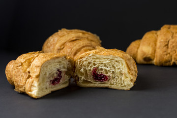 Golden croissant with cherry jam on a dark background