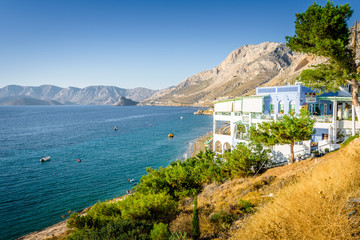 Beautiful sunny holiday view to the greek beach blue sea with crystal clear water beach with some boats fishing cruising surrounded by hills mountains, Kalymnos Island, Kos, Dodecanese, Greece 