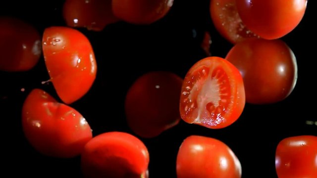 Whole and halves of tomatoes with juice bouncing against to the camera on a black background in slow motion