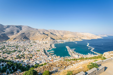 Beautiful sunny coast view to the greek blue sea with crystal clear water to the traditional town of Pothia surrounded by hills mountains with boats in harbor, Kalymnos Island, Kos, Dodecanese Greece
