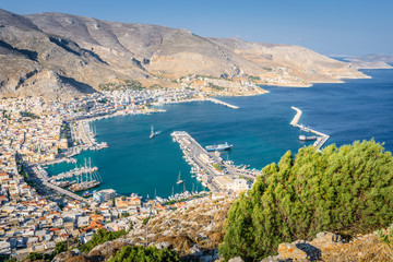 Beautiful sunny coast view to the greek blue sea with crystal clear water to the traditional town of Pothia surrounded by hills mountains with boats in harbor, Kalymnos Island, Kos, Dodecanese Greece