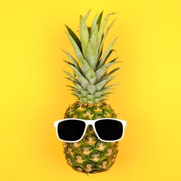 Hipster pineapple with sunglasses. Top view against a yellow background. Minimal summer concept.