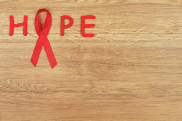 Oncological disease concept. Word "hope" written with a red ribbon - hiv / aids awareness sign on wooden background