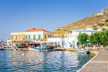 Obraz premium Beautiful sunny greek village town harbor view to the aegean blue sea with crystal clear water boats cruising surrounded by hills mountains windmills, Agia Marina, Leros Island, Dodecanese, Greece