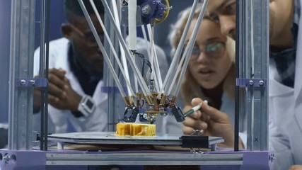 Interested multiethnic scientists gathering around 3-D printer and watching process of model production in laboratory.