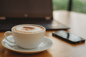 Coffee cup, laptop and smartphone on the wood table in cafe. Business concept