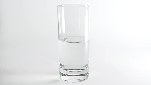 Two pieces of ice falling into transparent glass of water on white background. Slow motion.