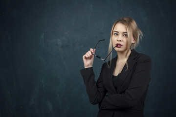 Portrait of a beautiful woman with sunglasses in hands and suit against a blue textural wall with place for text.