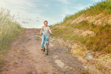 Naklejka premium Happy child riding bike. Young girl on bicycle in sunny summer park. Healthy school children summer activity. Kids playing and cycling outdoors. Little girl learns to keep balance while riding bicycle
