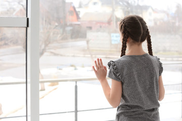 Lonely little girl near window indoors. Child autism