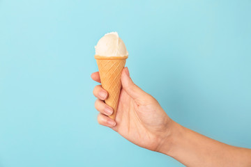 Woman holding waffle cone with tasty vanilla ice cream on color background