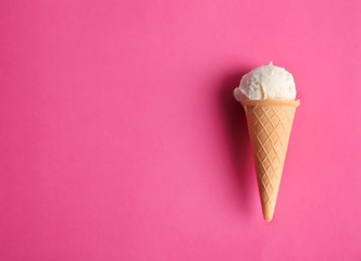 Waffle cone with tasty vanilla ice cream on color background