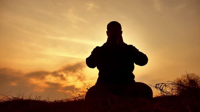 silhouette of a male monk engaged in meditation at sunset sunlight. Buddhist lifestyle prays at sunset healthy way of life nature