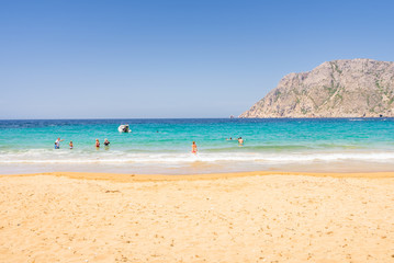 Beautiful sunny coast view to a cozy holiday bay with crystal clear blue water sandy beach for sunbathing and some boats cruising fishing in background, Patmos Island, Dodecanese/ Greece - 07 27 2017