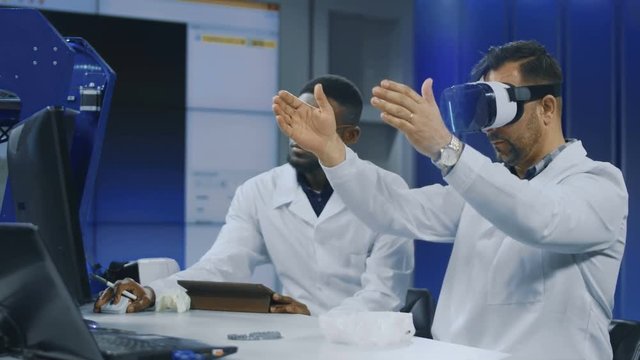 Multiracial Men In Medical Gowns Exploring 3d Scull Model In VR Glasses And Having Discussion. Movement Stabilized 4K Shot.