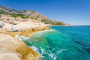 Beautiful sunny greek village town church and harbor view to the blue sea with crystal clear water and fishing boats cruising yacht at shore, Ikaria Island, Karkinagri, Sporades/ Greece – 08 01 2017