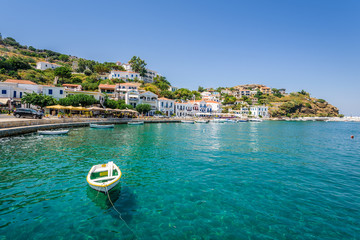 Beautiful sunny greek village town white house and harbor view to the aegean blue sea with crystal clear water and fishing boats cruising yacht white houses, Ikaria Island, Evdilos, Sporade, Greece - obrazy, fototapety, plakaty
