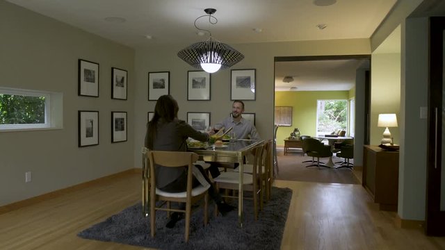 Mature couple eating meal and drinking red wine in open plan dining room. 