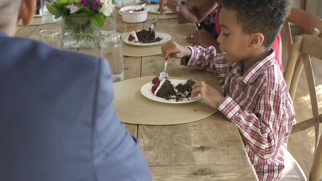 Medium shot of little boy eating cake with his family