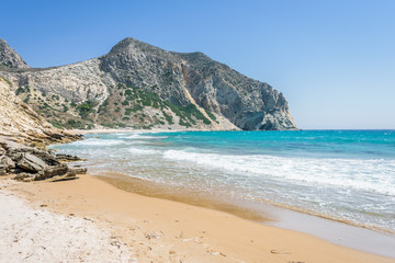 Fototapeta na wymiar Beautiful sunny coast view to the greek mediterranean blue sea with crystal clear water and pure sandy beach empty place with some mountains rocks surrounded, Kos, Dodecanese Islands, Greece
