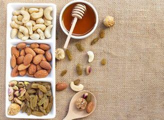 Dried fruits and variety of nuts in a dish with honey in a bowl on the wooden table.