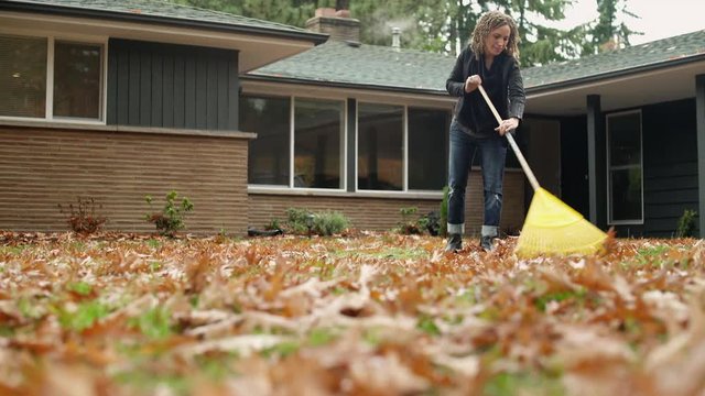 Woman raking leaves in garden, panning right.  