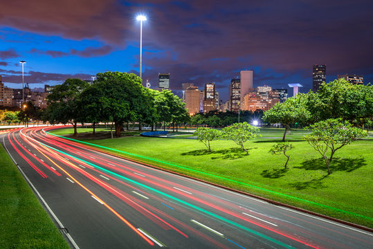 Four Lane Highway Crossing Flamengo Park at Night With Light Trails From Vehicles, and Rio de Janeiro City Downtown in the Horizon