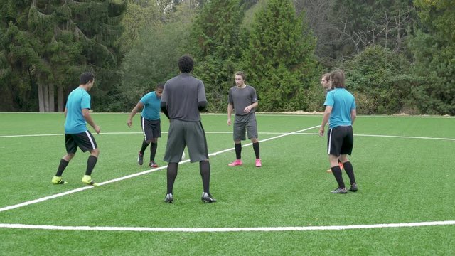 Male soccer players standing in circle passing ball.