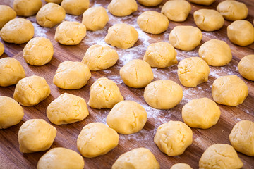 A close-up of the cheese pastry round buns before baking in straight rows on flour and a wooden table