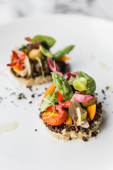 Quinoa canapes topping with pan seared asparagus, tomato and baby vegetables and olive oil served on white plate.