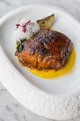 Pan seared trout. served with yellow sauce, foam amd roasted sliced onion on curved white plate. 