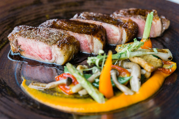 Roasted medium rare wagyu beef served with sour sauce with roasted baby vegetables on stone plate.