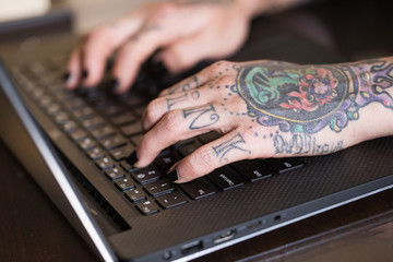 Tattooed hands typing on a laptop