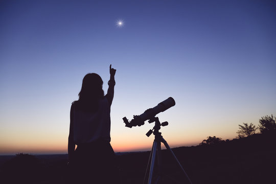 Young woman looking at the sky with a astronomical telescope.